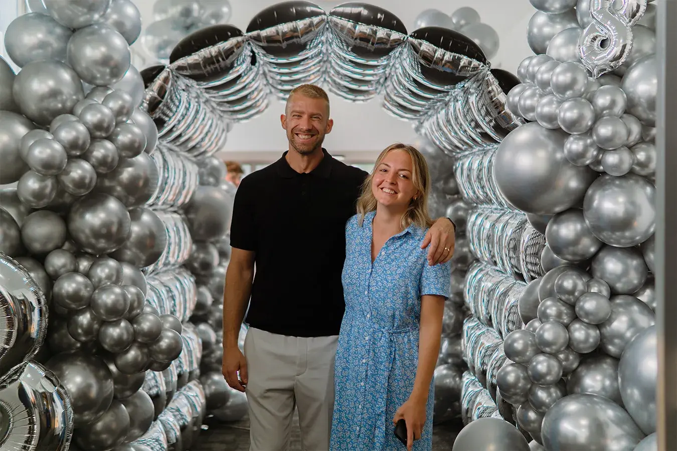 Two guests photographed in front of the chrome balloon wall