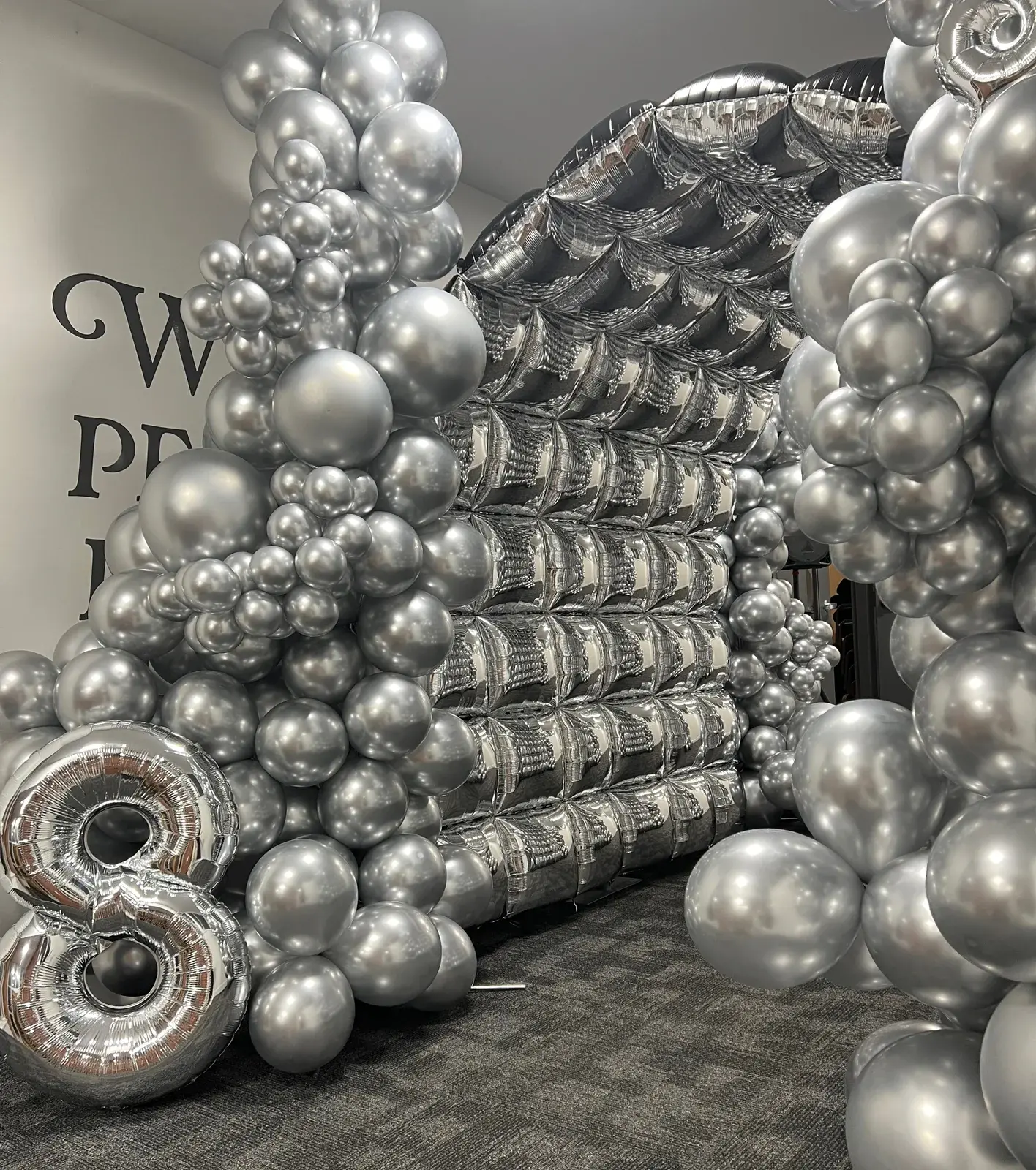 A full height silver chrome balloon wall with an oversized number eight