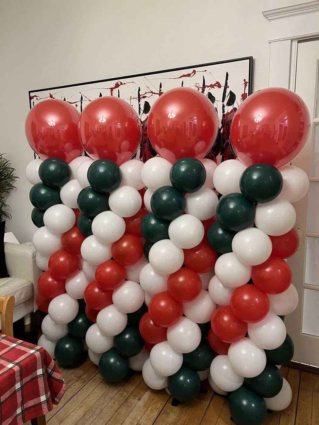Red, green and white balloon wall built against a wood panelled backdrop