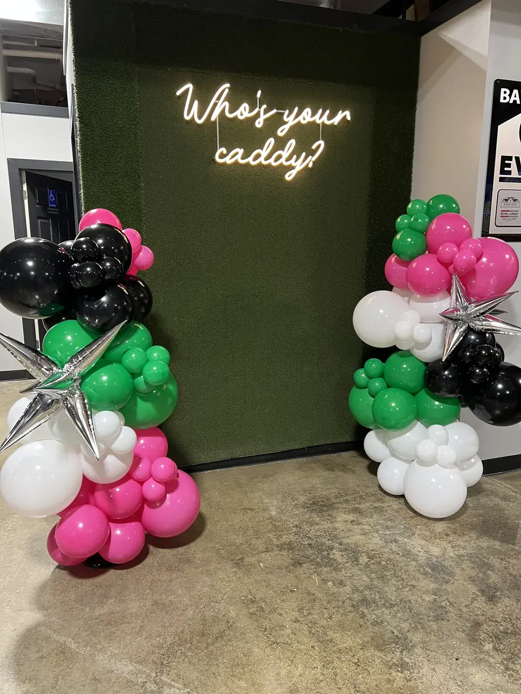 Who's your caddy neon on a green backdrop with pink, green and black columns