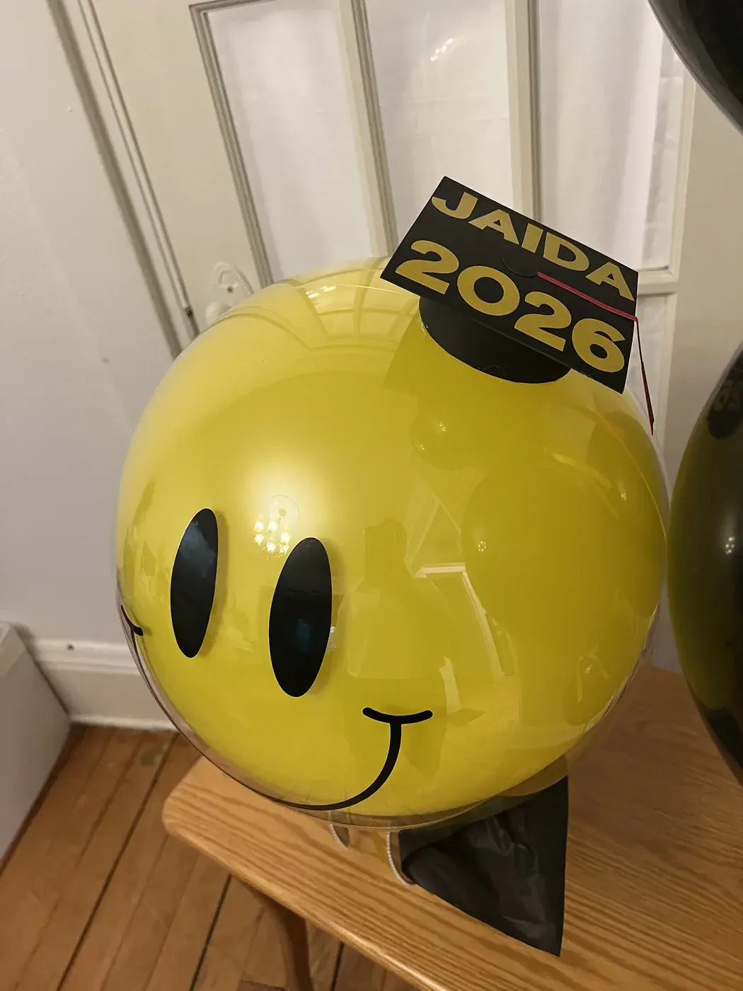 Oversized yellow smiley balloon in a graduation cap with a black balloon bouquet