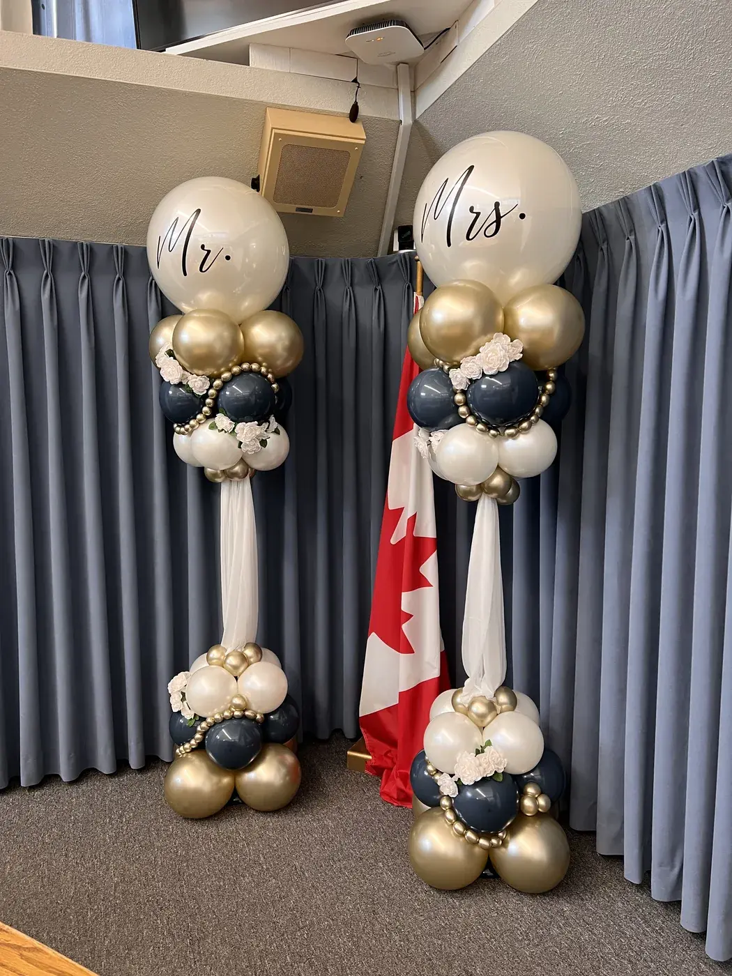 Mr and Mrs balloon columns in ivory, navy and gold either side of a Canadian flag