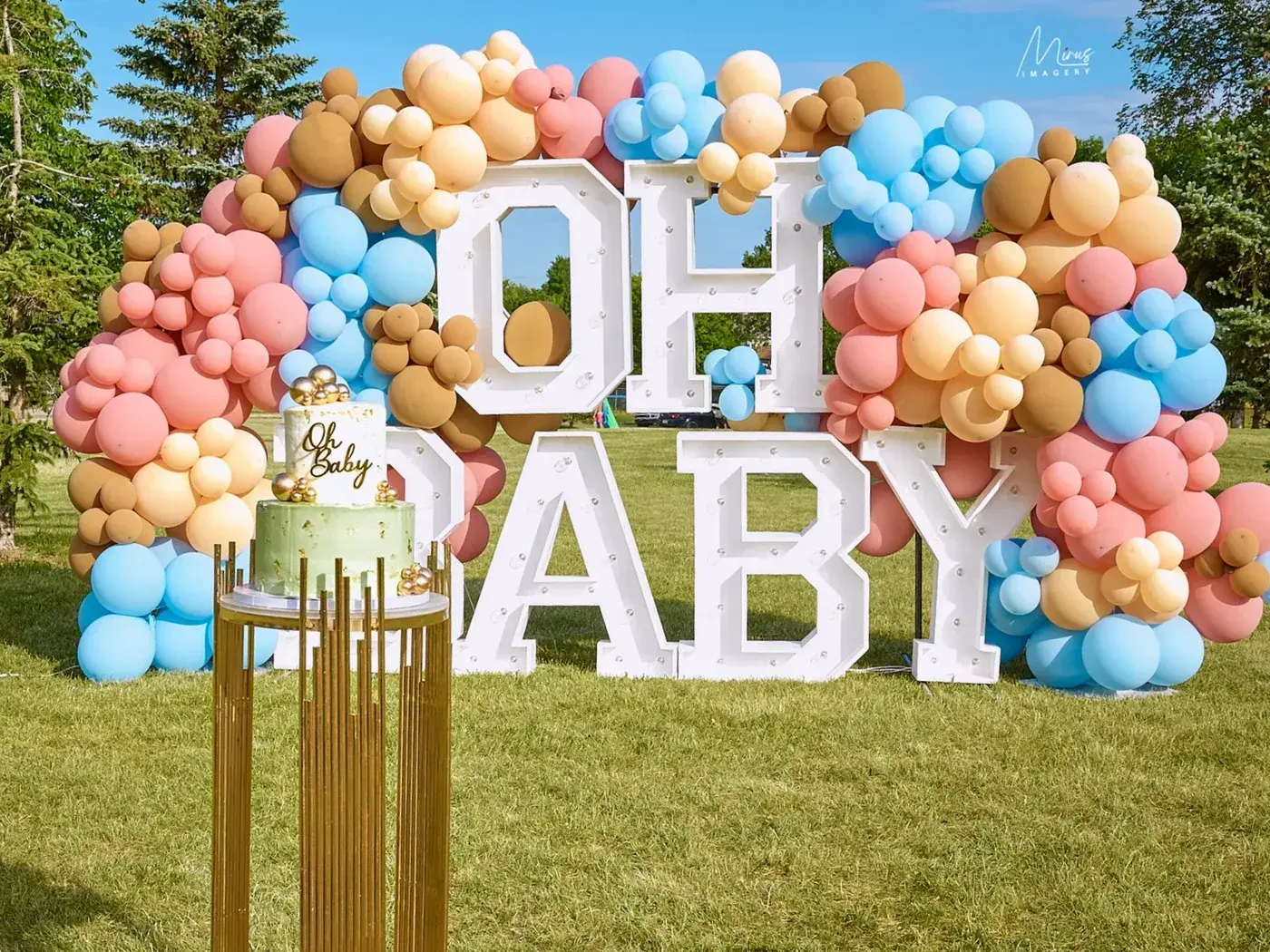 OH BABY marquee letters outdoors with a peach and sage garland and a cake plinth