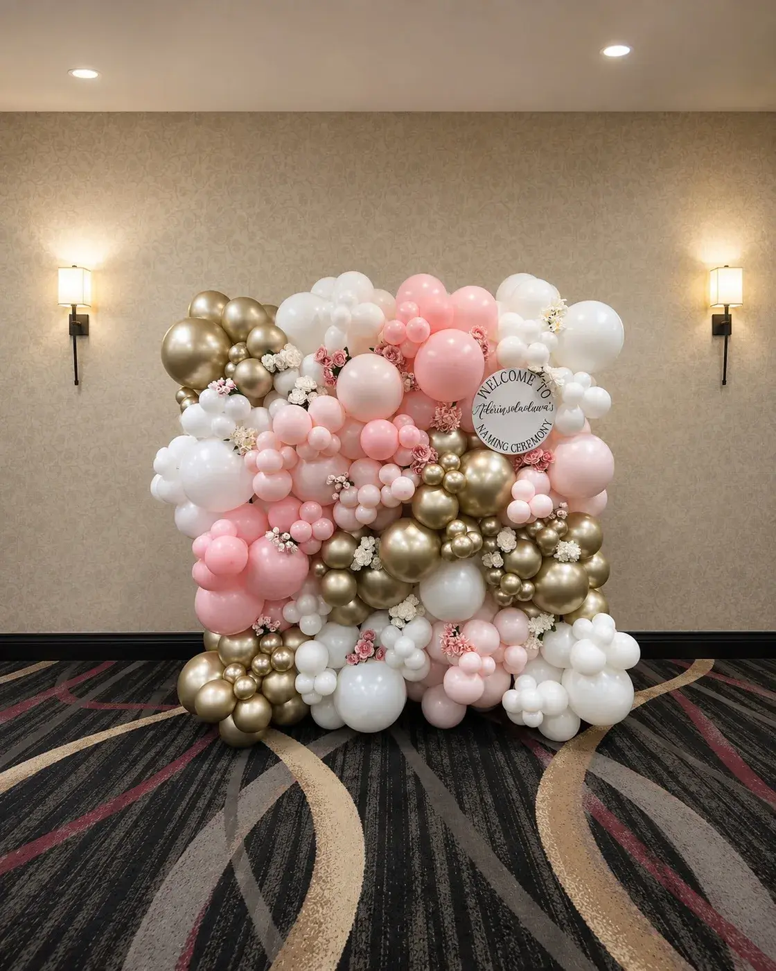 Pink, white and gold balloon wall with a naming ceremony welcome sign