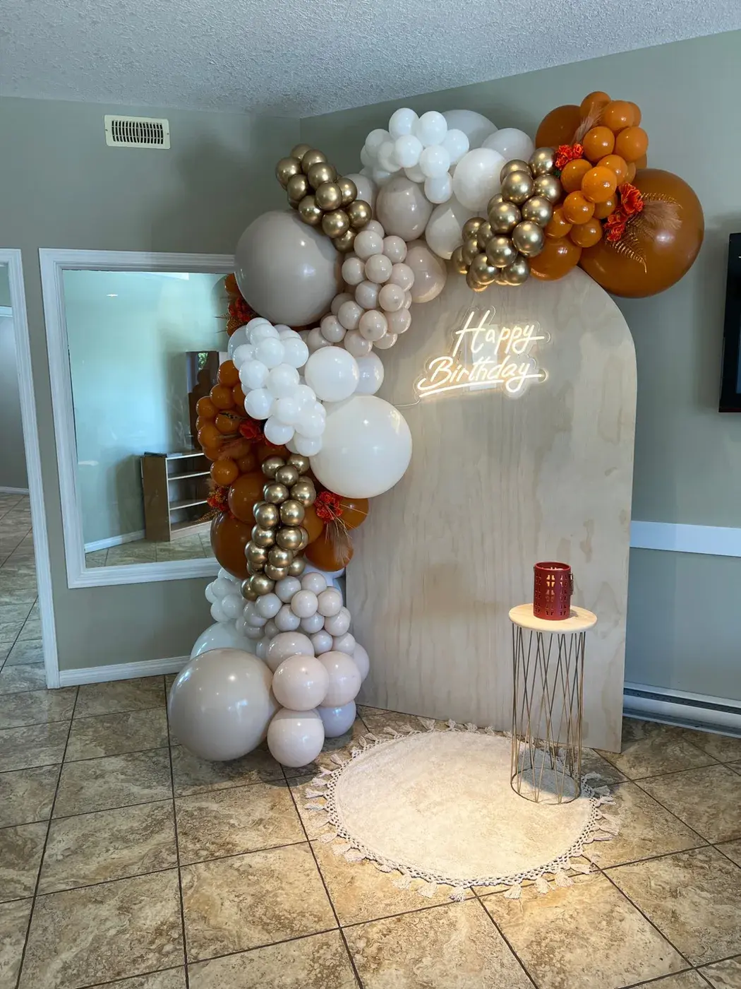 Wood grain wall with a cream, rust and copper garland, a neon sign and a cake plinth