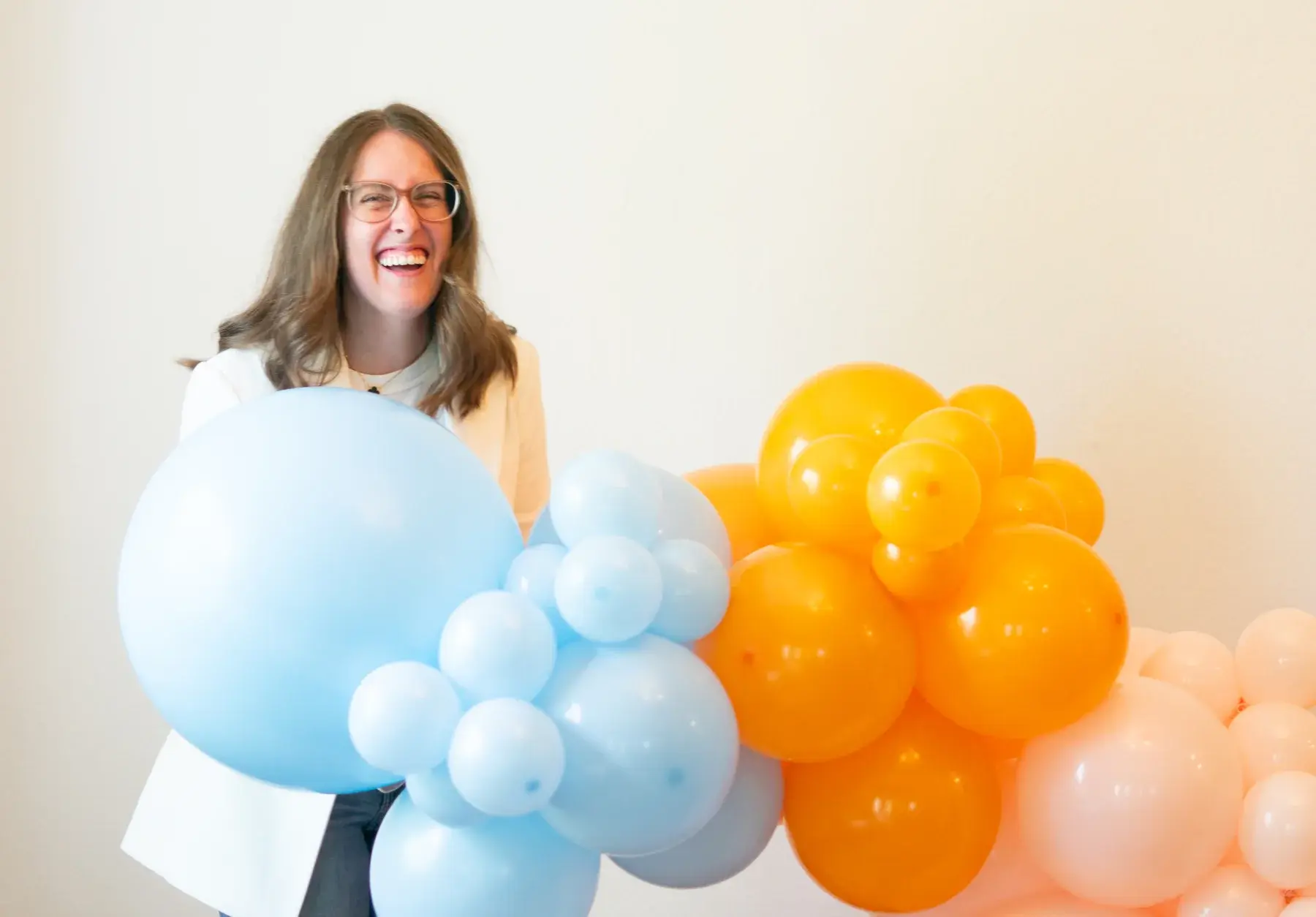 Rebecca laughing while holding an oversized pale blue balloon in front of an orange and blue garland