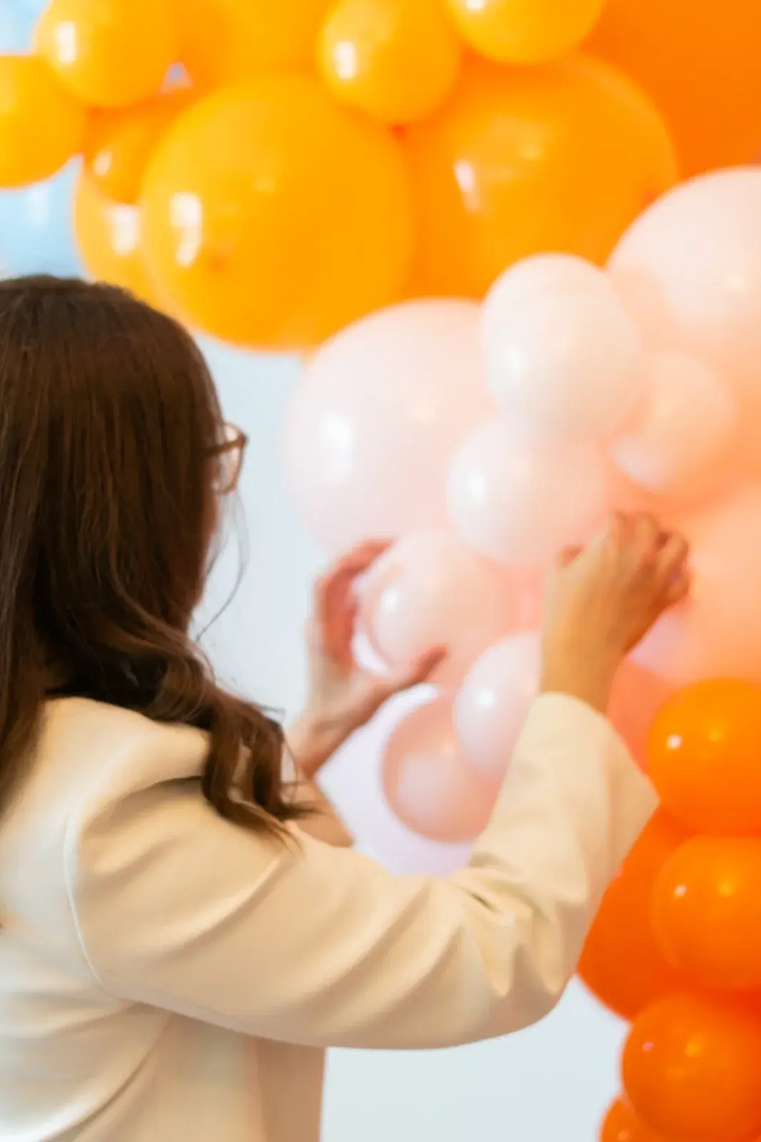 Rebecca placing balloons into a peach and orange garland on a wall